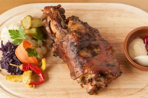 Roasted european pork knuckle on wood platter with vegetable garnish.